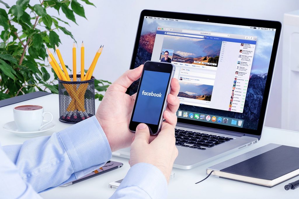 A person uses Facebook with a mobile phone and a laptop at the same time.