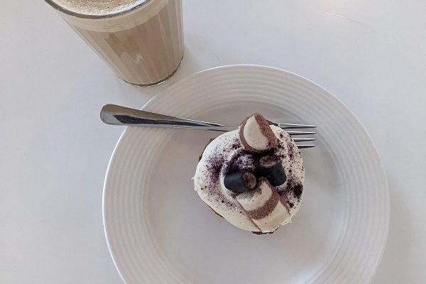 A cap cake with cream and marshmallows and a caramel latte with heart latte art on the white table