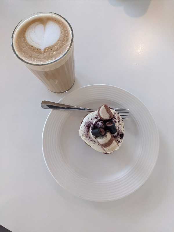 A cap cake with cream and marshmallows and a caramel latte with heart latte art on the white table 