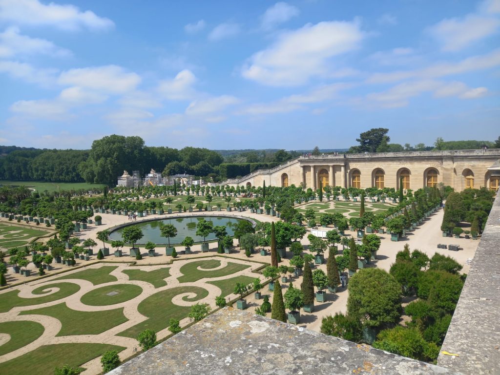 Castle and gardens of Versailles in France.In the picture there are a fountain and trees in the gardens.
