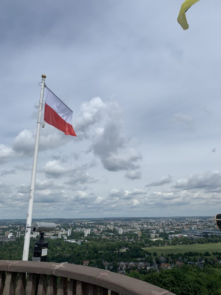 A beautiful view across the city of Krakow. There is a flag of Poland and a telescope.