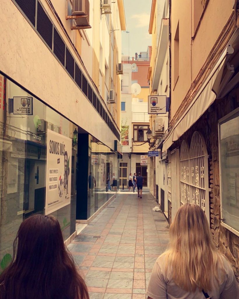 two girls walking in the street of Fuengirola town. The street is narrow alley that has stores both sides.