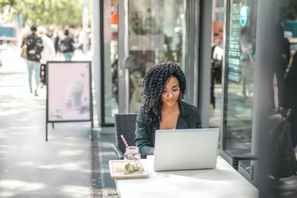 Woman using a laptop on the terrace of a cafe. The terrace is located on a busy shopping street.