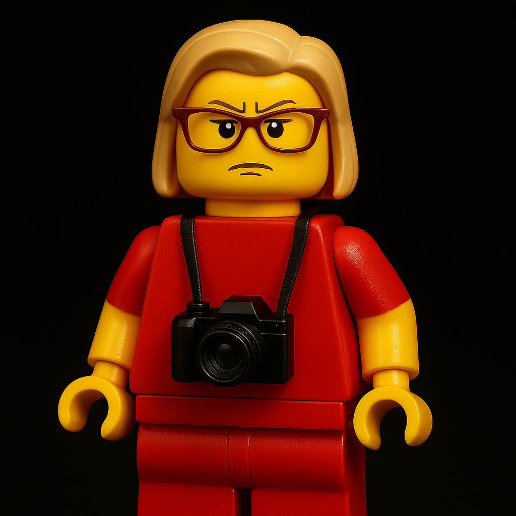 An angry looking female Lego-character who is wearing glasses and with a DSLR camera hanging around her neck.