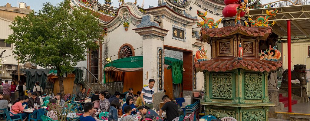 Many people sitting and chatting in front of a temple in Tainan