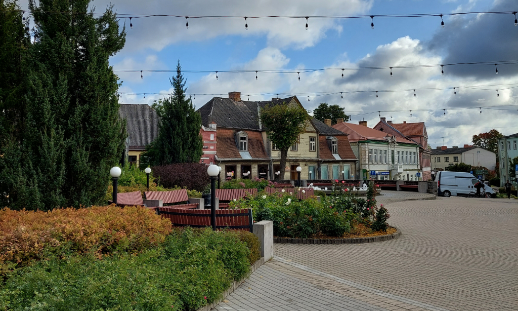 Garden area in the old market square of Tukums with buildings in the back.