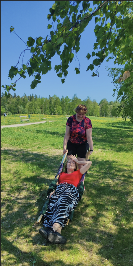 Lavastetussa tilanteessa henkilö kannattelee paarien pääpuolta samaan aikaan kun toinen henkilö makaa niillä pidellen kättä otsallaan.