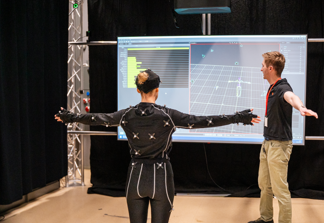 Motion capture setup with an actor in a sensor suit performing a T-pose while being guided by another person.
