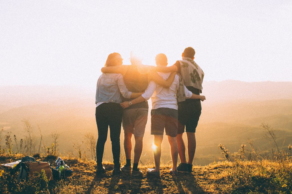 Four people are hugging each other while watching the sunset.