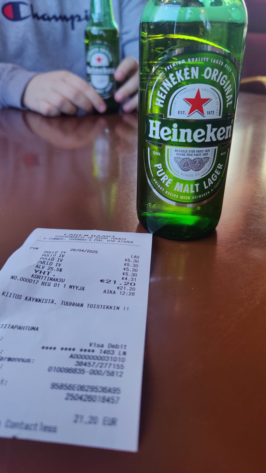 Pullo Heineken olutta ja kuitti, jossa sanotaan "kiitos käynnistä, tuuhhan toistekkin!!". Neljä Heineken olutta maksoi 21.20€.