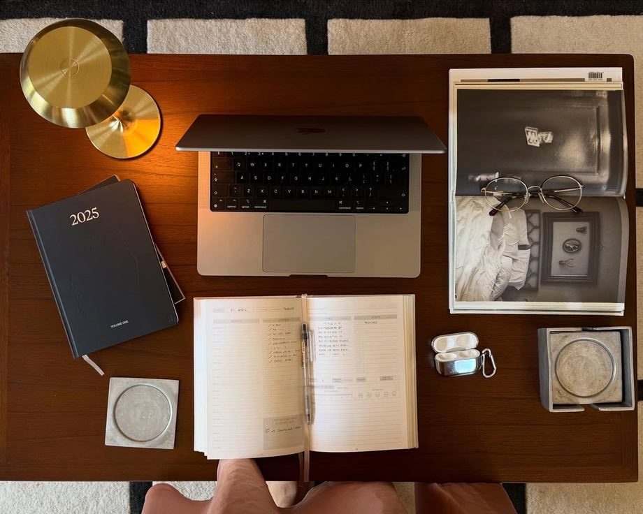 Organisoitu työpöytä, jolla on kannettava tietokone, kalenteri, vihko, kuulokkeet ja silmälasit